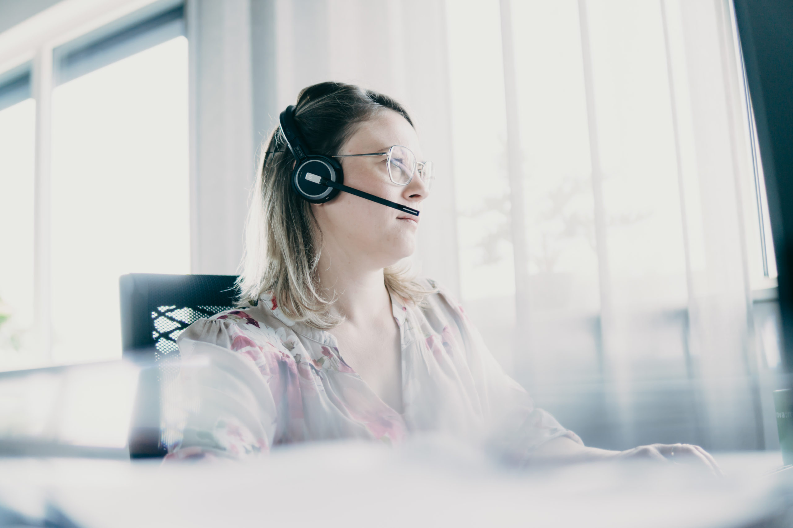Nova:med Support Mitarbeiterin sitzt am Schreibtisch mit einem Headset auf dem Kopf
