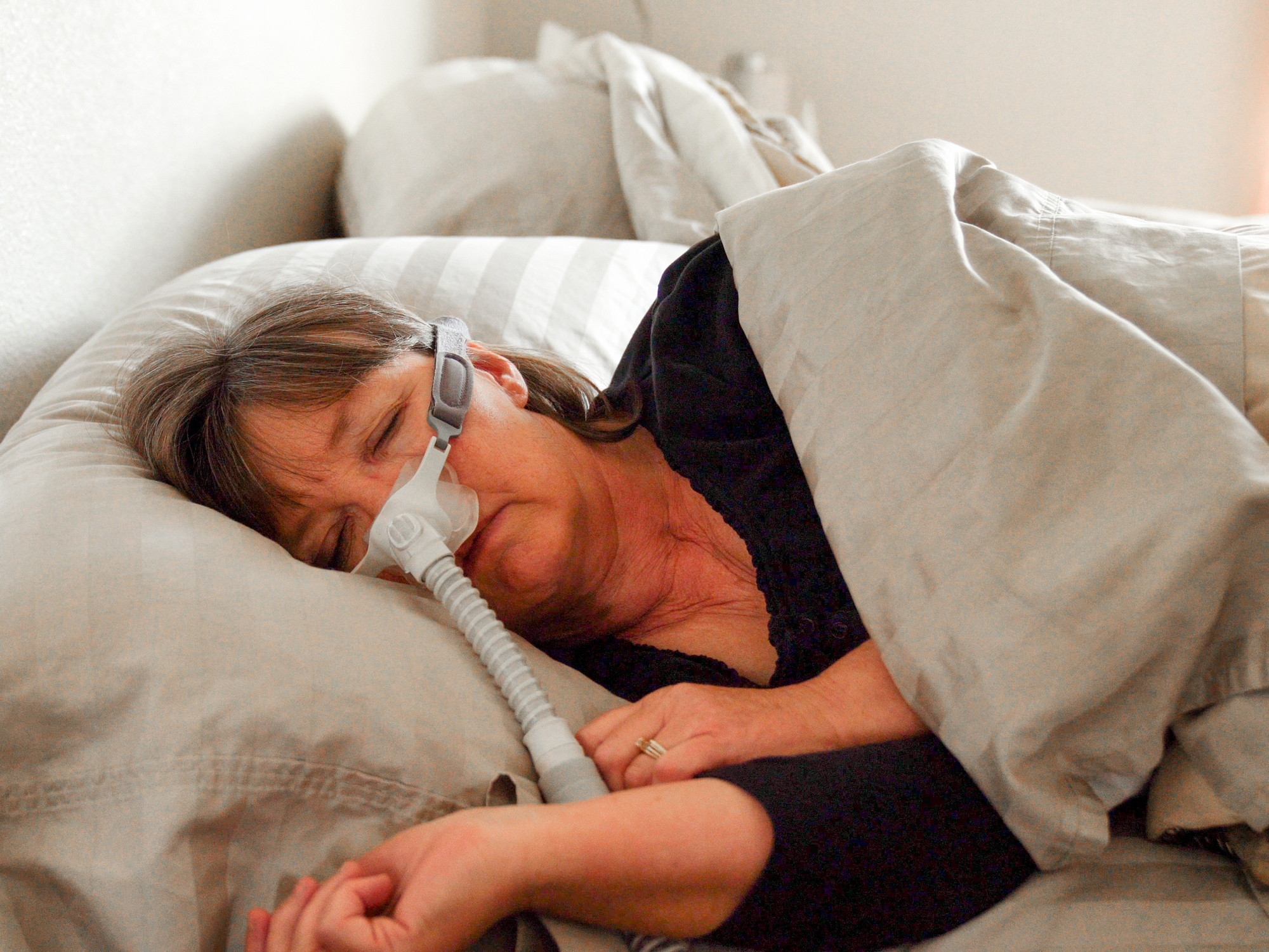 Frau mittleren Alters mit Schlafapnoe schläft in einem Bett und trägt ein CPAP-Gerät (Continuous Positive Airway Pressure), um ihr beim Schlafen zu helfen